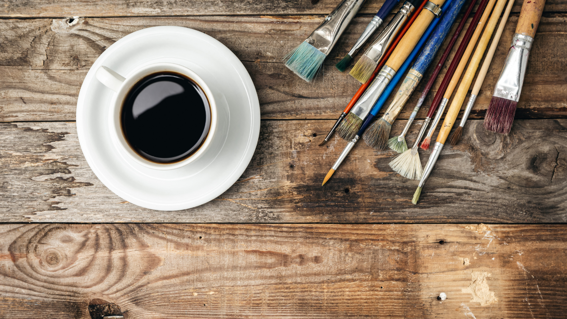 Wooden background with paint brushes and a cup of coffee