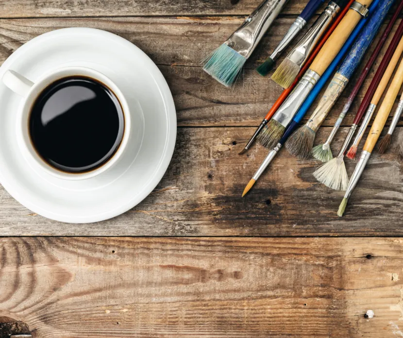Wooden background with paint brushes and a cup of coffee